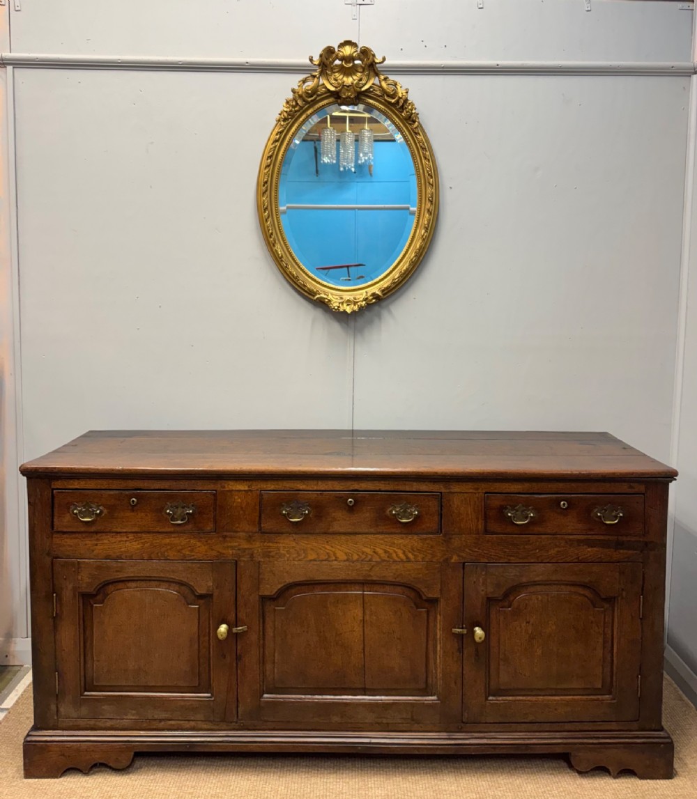 An 18th-century Georgian oak dresser base featuring three top drawers with brass drop handles above three cupboard doors with fielded arched panels. View II