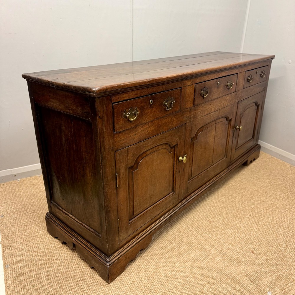 An 18th-century Georgian oak dresser base featuring three top drawers with brass drop handles above three cupboard doors with fielded arched panels. View III