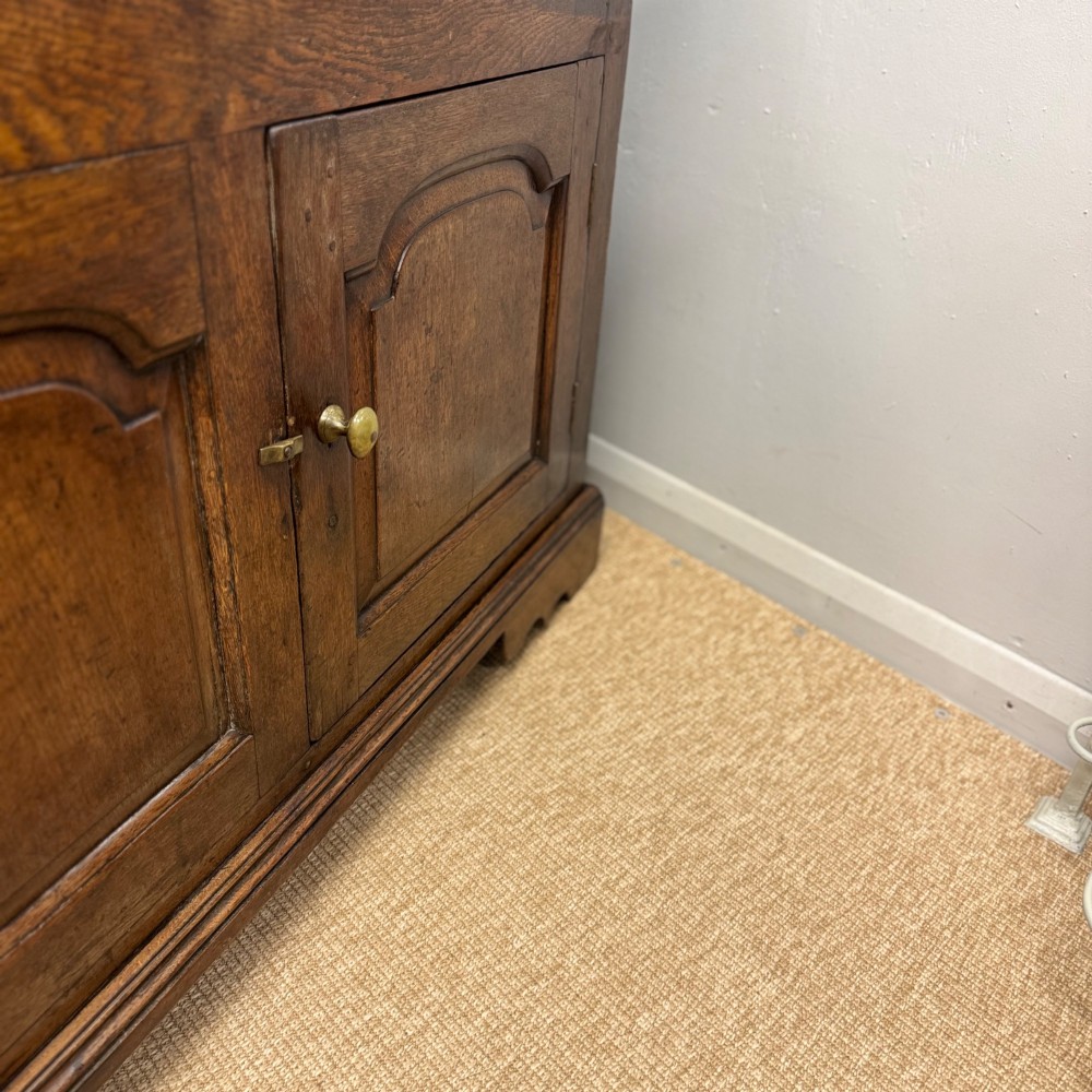 An 18th-century Georgian oak dresser base featuring three top drawers with brass drop handles above three cupboard doors with fielded arched panels. View IV