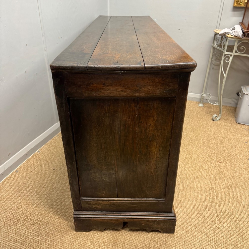 An 18th-century Georgian oak dresser base featuring three top drawers with brass drop handles above three cupboard doors with fielded arched panels. View V
