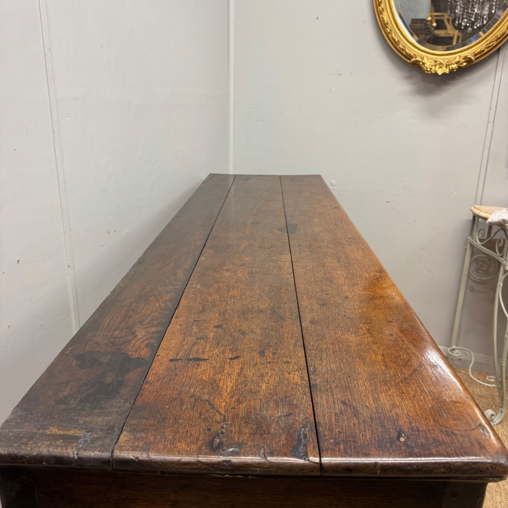 An 18th-century Georgian oak dresser base featuring three top drawers with brass drop handles above three cupboard doors with fielded arched panels. View VII