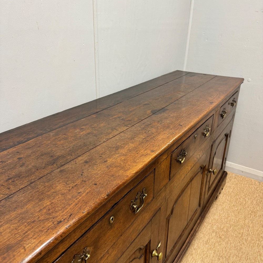 An 18th-century Georgian oak dresser base featuring three top drawers with brass drop handles above three cupboard doors with fielded arched panels. View VIII