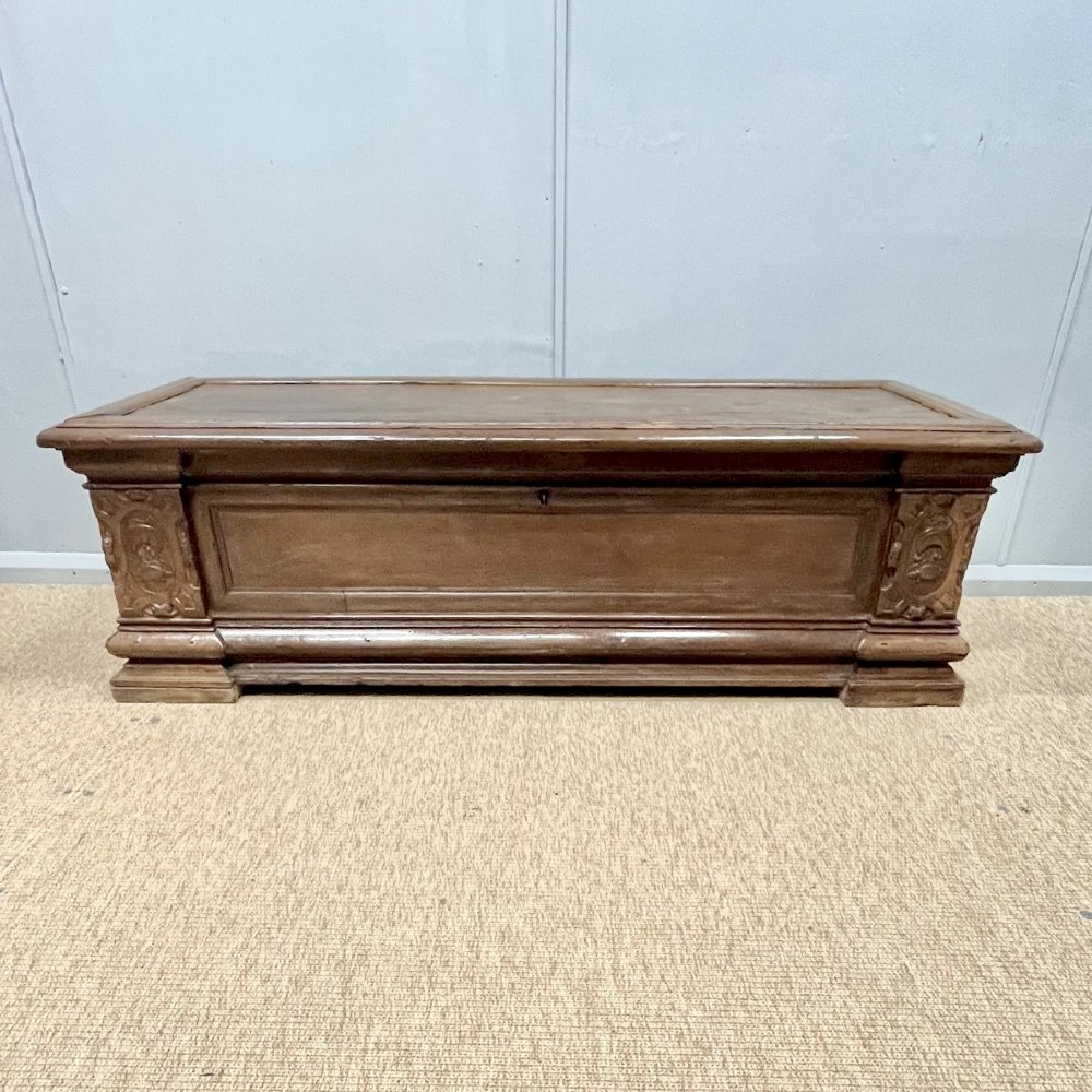 A large 17th-century Italian walnut marriage chest featuring carved corner pilasters, recessed front panels, and a plinth base.
