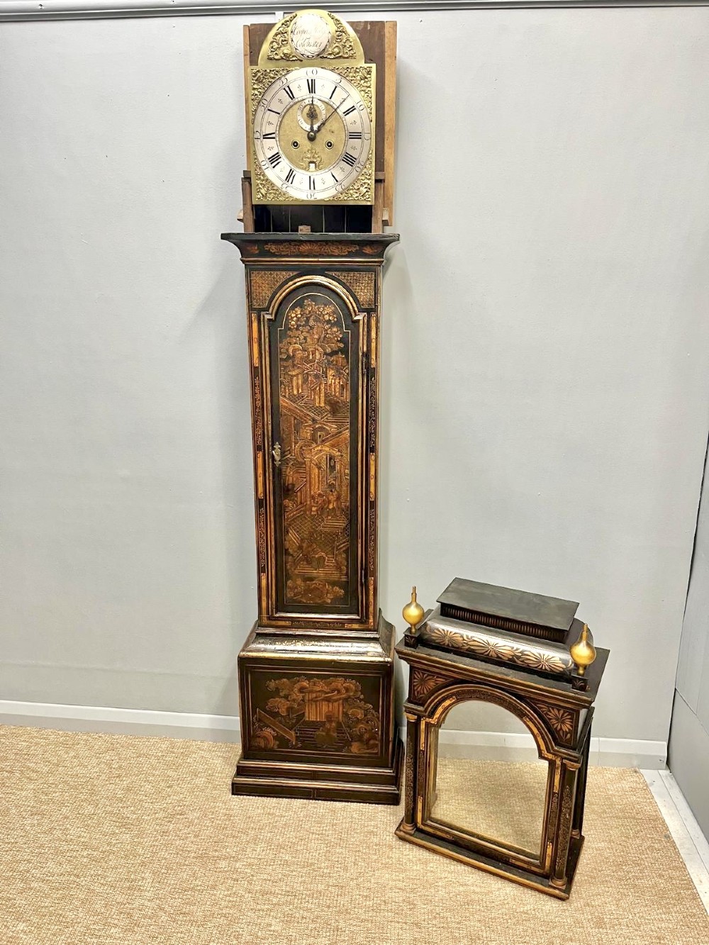 An 18th-century black lacquered longcase clock featuring gilt chinoiserie artwork, brass finials, and an arched brass dial. View II