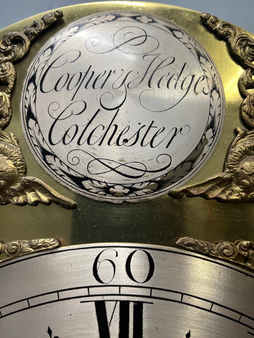 An 18th-century black lacquered longcase clock featuring gilt chinoiserie artwork, brass finials, and an arched brass dial. View V