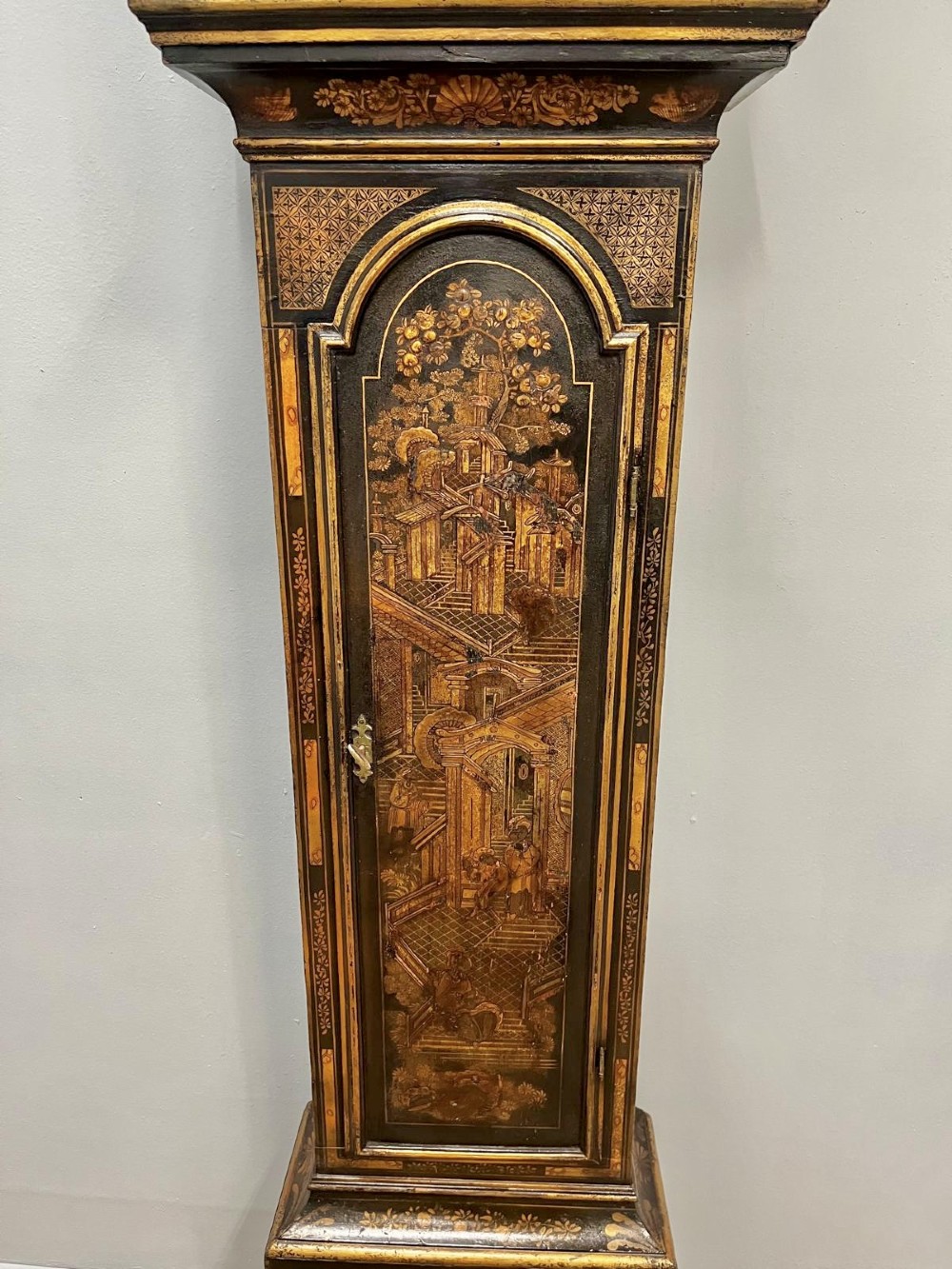 An 18th-century black lacquered longcase clock featuring gilt chinoiserie artwork, brass finials, and an arched brass dial. View IX