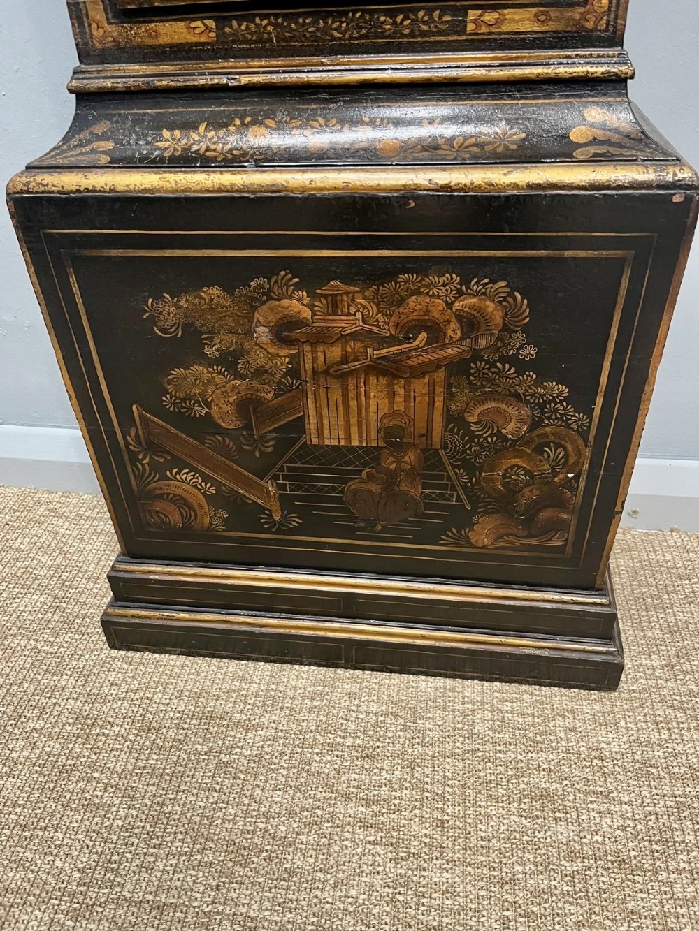 An 18th-century black lacquered longcase clock featuring gilt chinoiserie artwork, brass finials, and an arched brass dial. View X