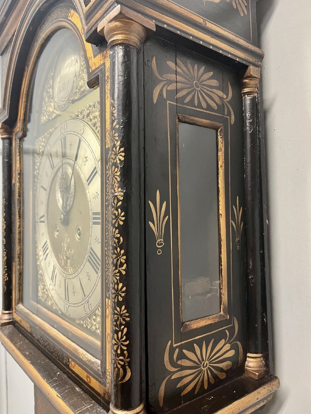 An 18th-century black lacquered longcase clock featuring gilt chinoiserie artwork, brass finials, and an arched brass dial. View XI