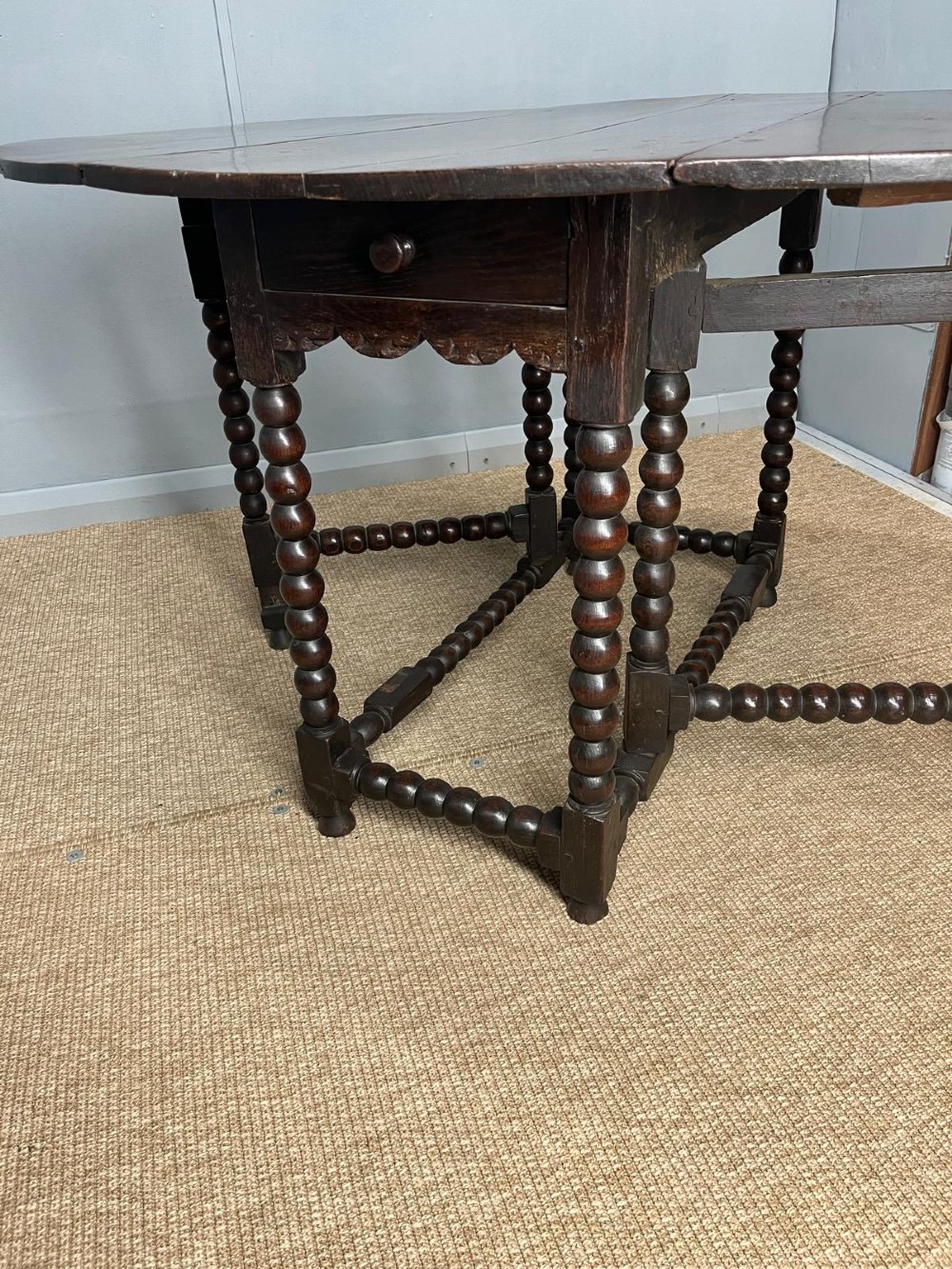 A dark oak gateleg table featuring an oval drop-leaf top, bobbin-turned legs, and matching turned stretchers. View V