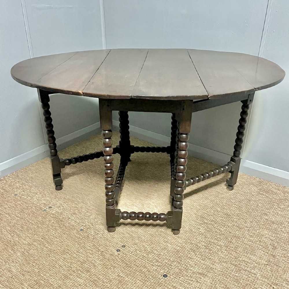 A dark oak gateleg table featuring an oval drop-leaf top, bobbin-turned legs, and matching turned stretchers.