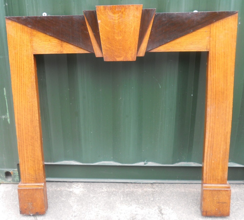 An Art Deco oak fire surround featuring contrasting dark wood triangular inlays and a prominent central keystone motif.