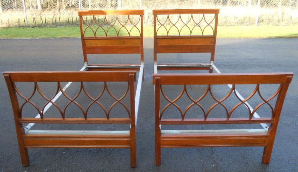 A pair of Edwardian inlaid mahogany single bed frames featuring geometric openwork headboards and footboards.