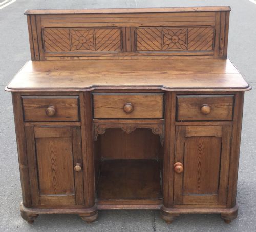 fig 1. Victorian pitch pine kneehole writing desk featuring a carved gallery back, three frieze drawers, two cupboard doors, and wooden knob handles.
