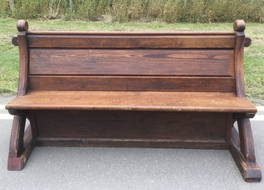 A Victorian pitch pine church bench featuring a solid plank seat, panelled backrest, and shaped side end frames.