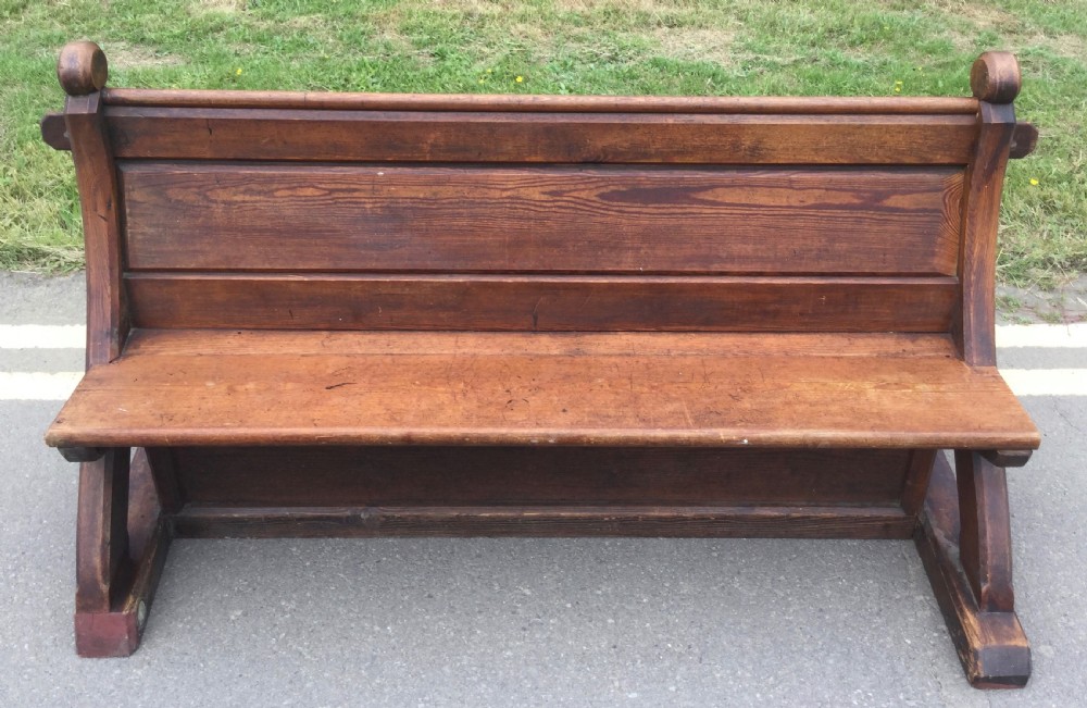 A Victorian pitch pine church bench featuring a solid plank seat, panelled backrest, and shaped side end frames. View X