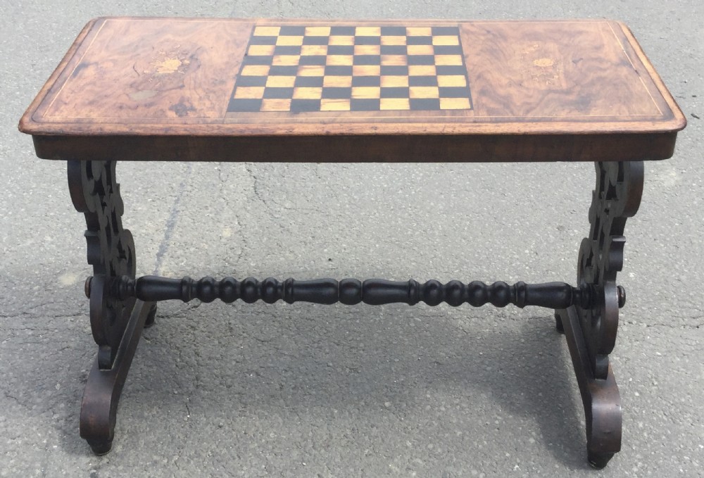 A rectangular Victorian walnut games table featuring a central inlaid chessboard, marquetry side panels, carved trestle ends, and a turned stretcher.