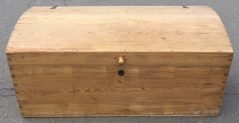 A large rectangular natural pine blanket chest with a rounded domed lid, corner dovetail joints, a central wooden knob, and an iron escutcheon.