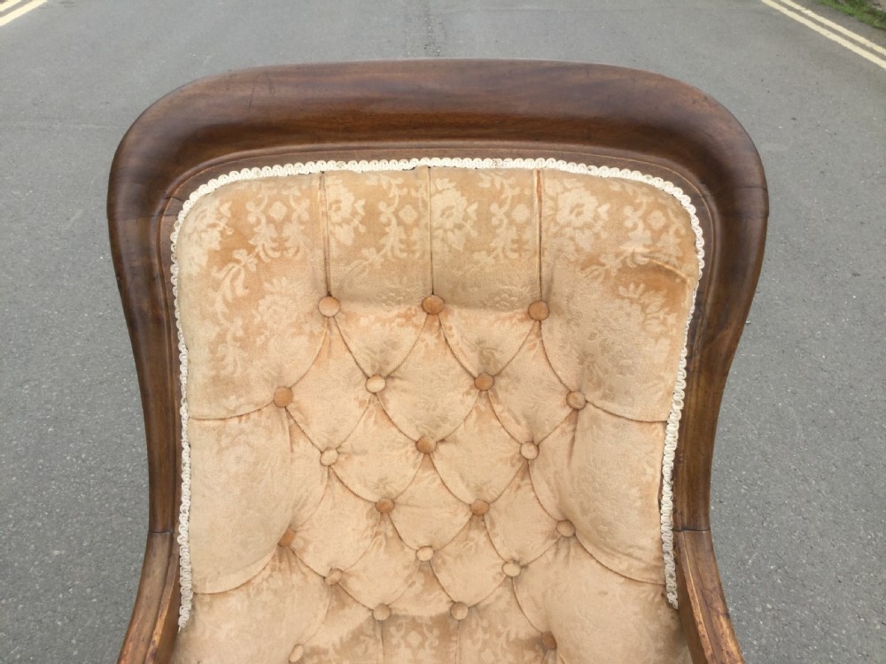 A Victorian mahogany open armchair upholstered in beige patterned fabric with deep button-tufting, padded armrests, and turned front legs on white ceramic castors. View IX
