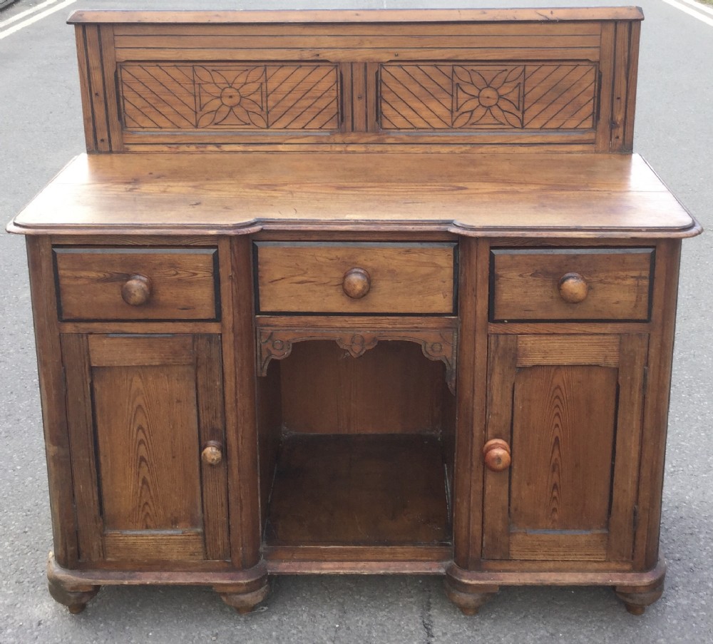 Victorian pitch pine kneehole writing desk featuring a carved gallery back, three frieze drawers, two cupboard doors, and wooden knob handles.
