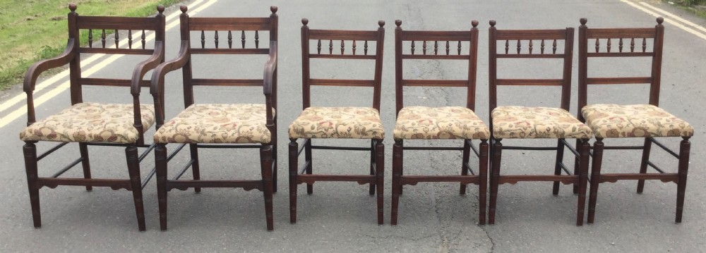 A set of six Edwardian mahogany dining chairs featuring upper spindle galleries, turned front legs, floral upholstered seats, and two matching carver armchairs.