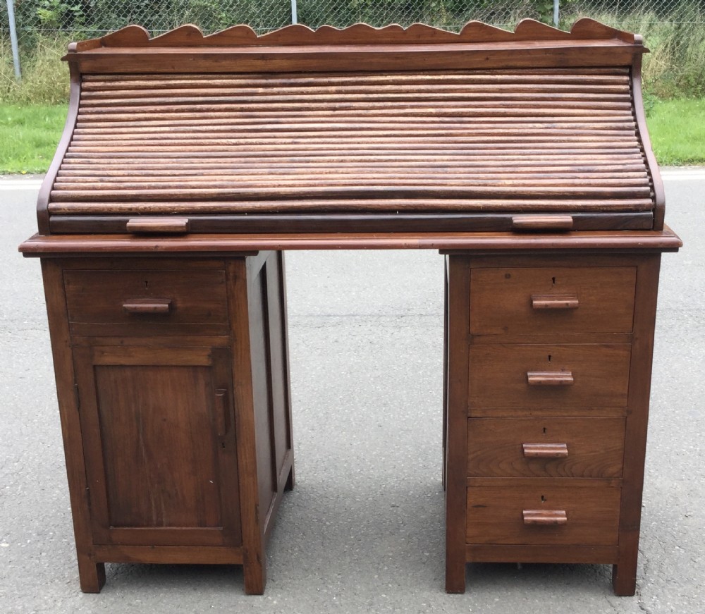 An Edwardian mahogany rolltop pedestal desk featuring a slatted tambour front, a scalloped top gallery, wooden handles, and a pedestal base with drawers and a cupboard.