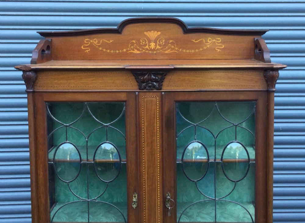An antique mahogany display cabinet with leaded glass doors, delicate marquetry inlay on the pediment, and slender cabriole legs. View III