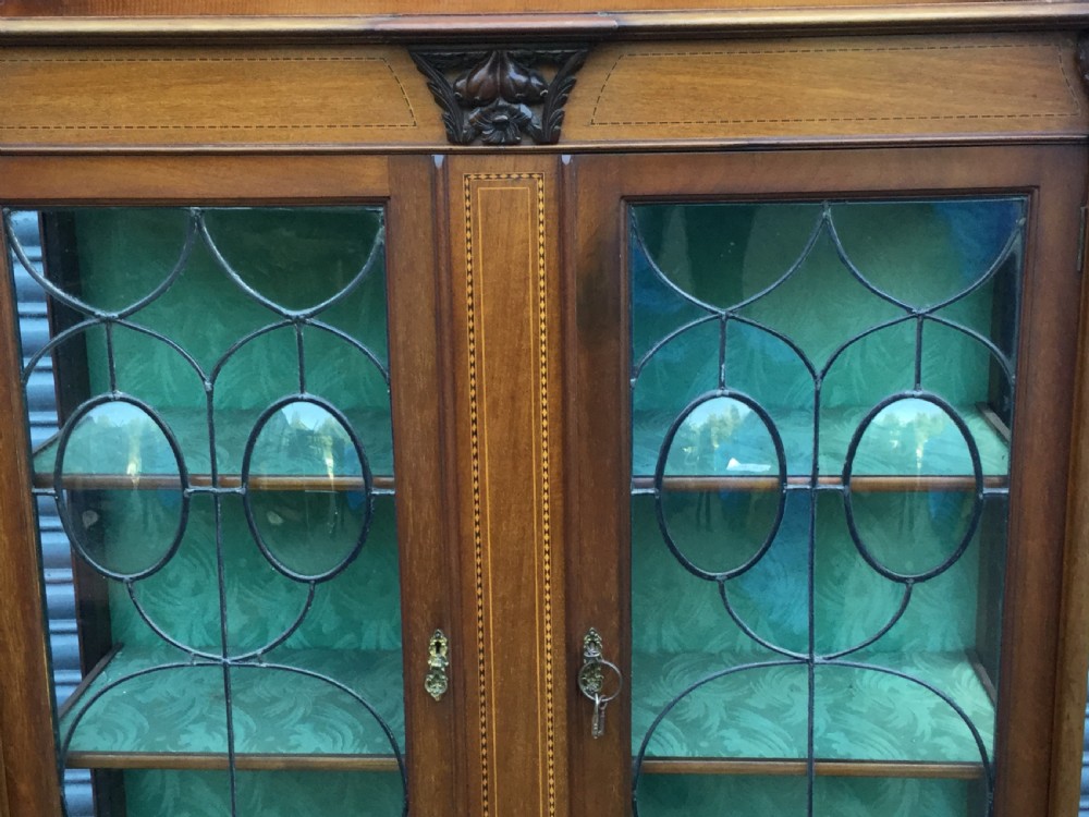 An antique mahogany display cabinet with leaded glass doors, delicate marquetry inlay on the pediment, and slender cabriole legs. View V