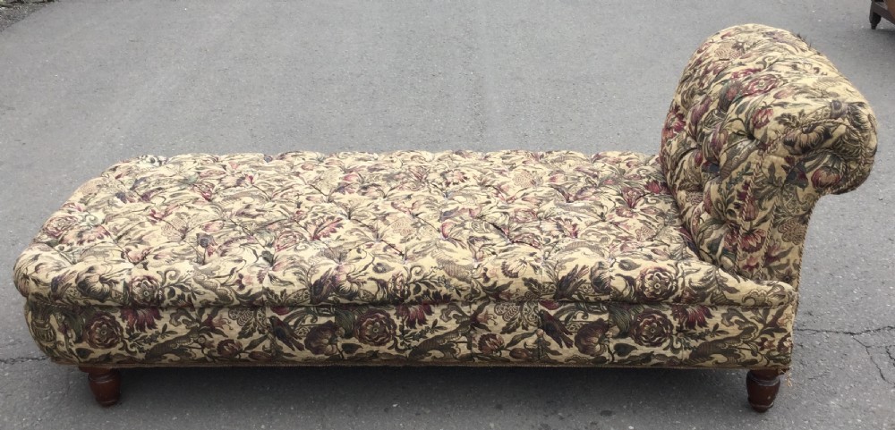 A Victorian upholstered daybed featuring deep-buttoned floral tapestry fabric with a scrolled end rest and turned wooden legs.