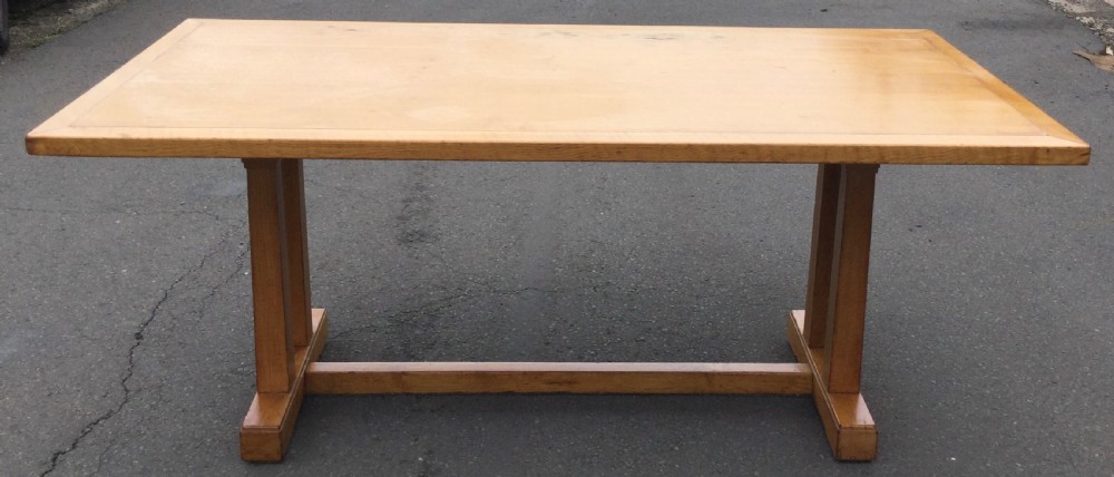 A rectangular golden oak refectory dining table featuring a framed top surface, twin vertical trestle leg supports, and a low central connecting stretcher.