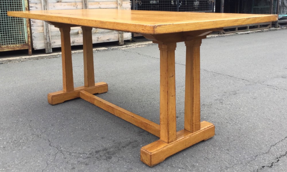 A rectangular golden oak refectory dining table featuring a framed top surface, twin vertical trestle leg supports, and a low central connecting stretcher. View III