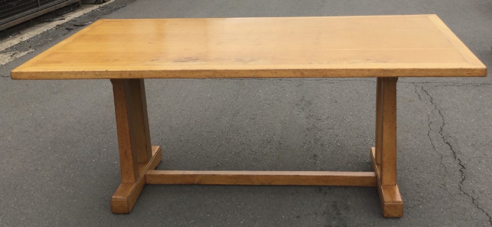 A rectangular golden oak refectory dining table featuring a framed top surface, twin vertical trestle leg supports, and a low central connecting stretcher. View VI