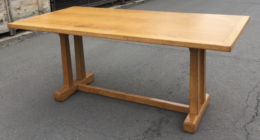 A rectangular golden oak refectory dining table featuring a framed top surface, twin vertical trestle leg supports, and a low central connecting stretcher. View VII