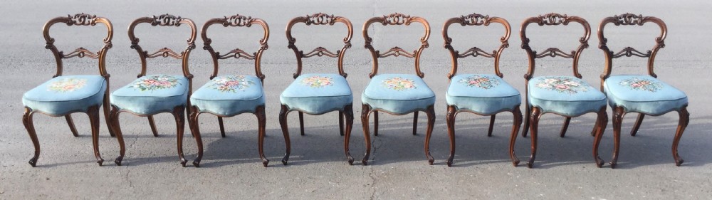 A set of eight Victorian walnut dining chairs featuring carved balloon backs, light blue velvet upholstered seats with central floral needlepoint designs, and cabriole front legs. View II