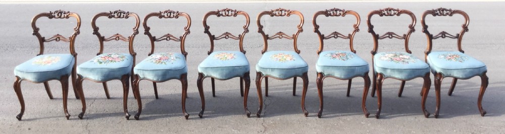 A set of eight Victorian walnut dining chairs featuring carved balloon backs, light blue velvet upholstered seats with central floral needlepoint designs, and cabriole front legs. View III