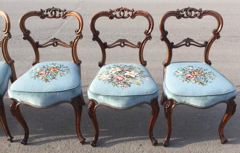 A set of eight Victorian walnut dining chairs featuring carved balloon backs, light blue velvet upholstered seats with central floral needlepoint designs, and cabriole front legs. View VI