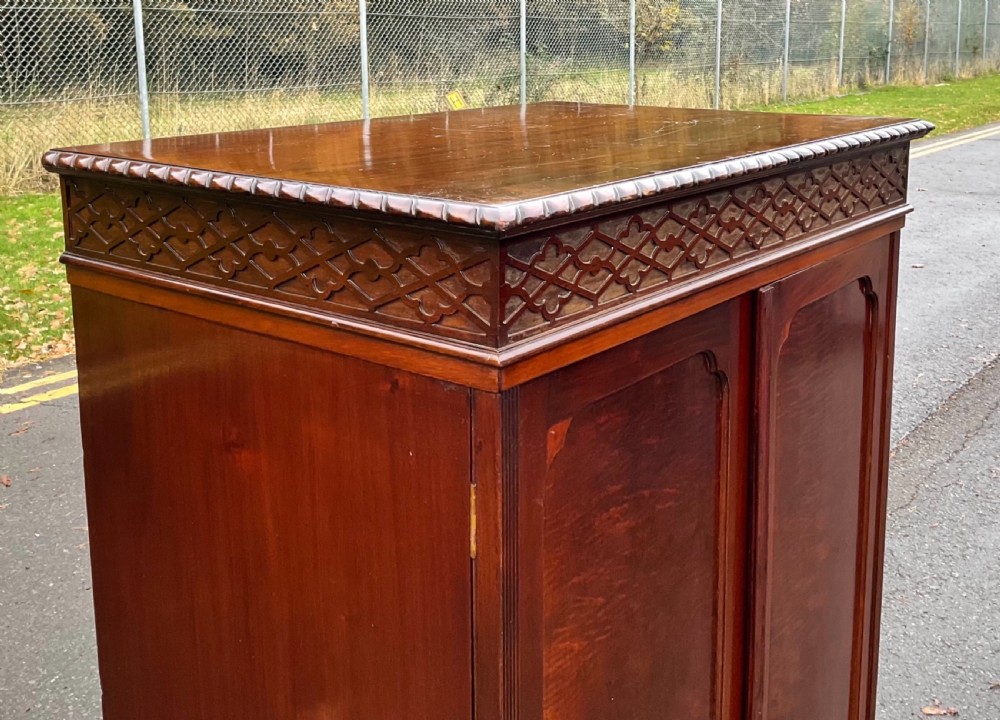A tall Chippendale style mahogany cabinet featuring carved blind fretwork on the top frieze, arched panel doors, and bracket feet. View IV