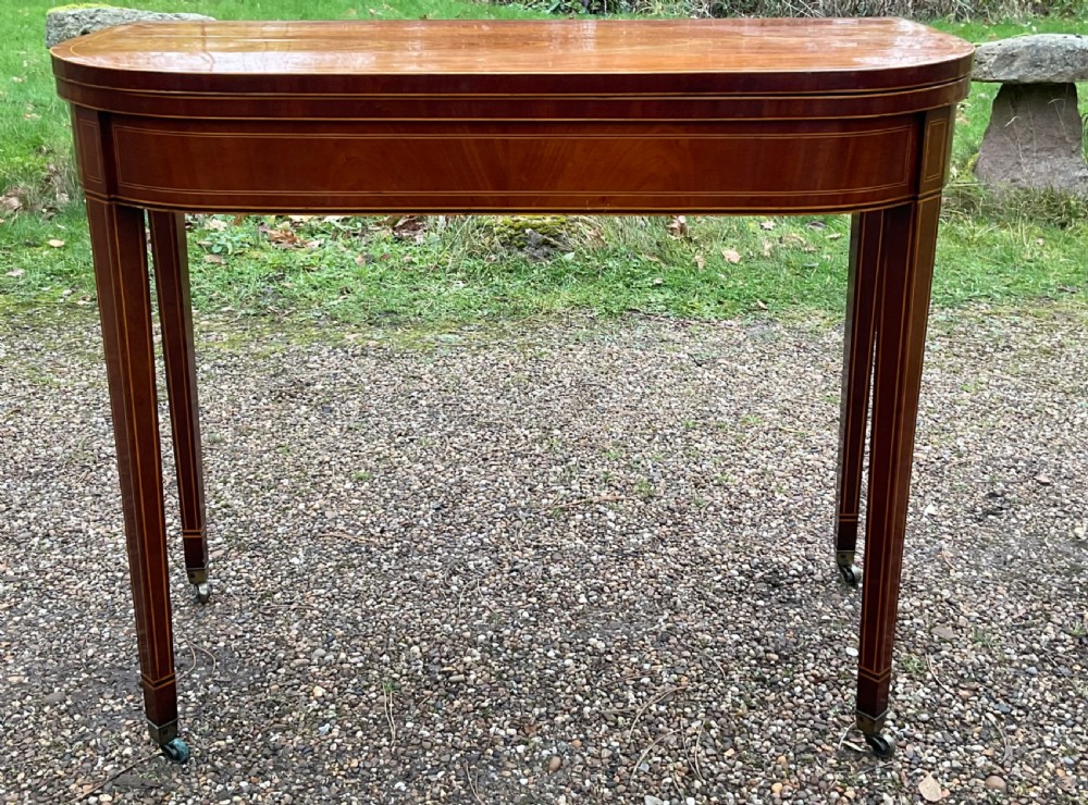 A Georgian inlaid mahogany foldover tea table featuring tapered square legs with brass castors and delicate geometric stringing along the frieze.