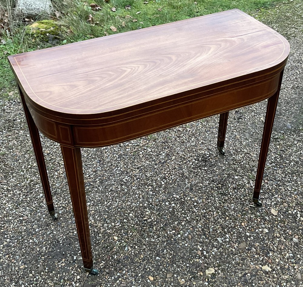 A Georgian inlaid mahogany foldover tea table featuring tapered square legs with brass castors and delicate geometric stringing along the frieze. View II
