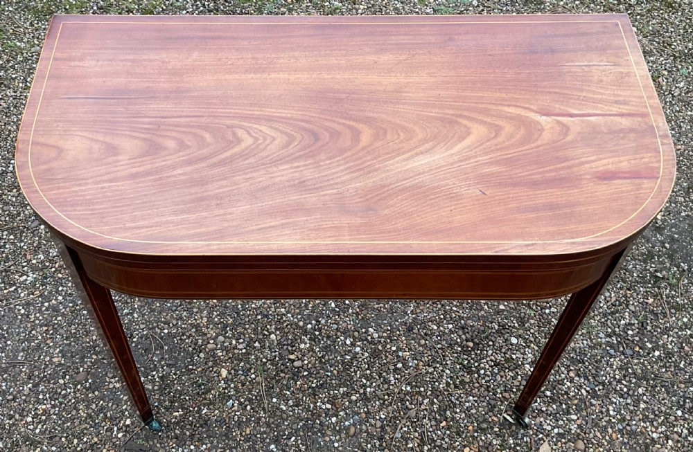 A Georgian inlaid mahogany foldover tea table featuring tapered square legs with brass castors and delicate geometric stringing along the frieze. View III