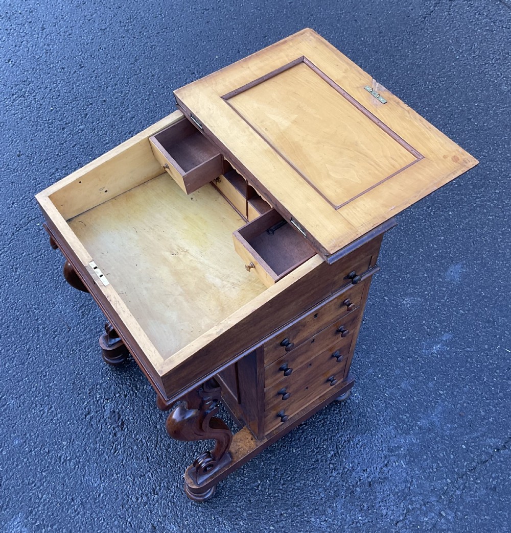 A Victorian walnut Davenport desk featuring a slanted writing surface with a green leather inset, side drawers with turned wooden knobs, and carved S-scroll front supports. View XIII