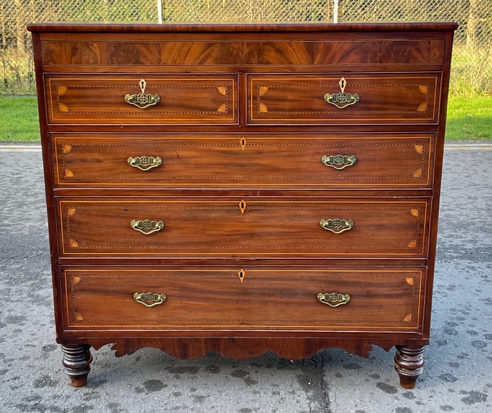 A Georgian mahogany chest of drawers with decorative boxwood inlay, brass handles, and turned foot supports.