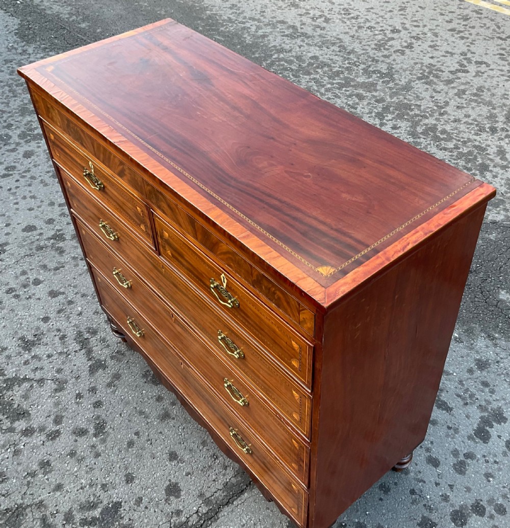 A Georgian mahogany chest of drawers with decorative boxwood inlay, brass handles, and turned foot supports. View V