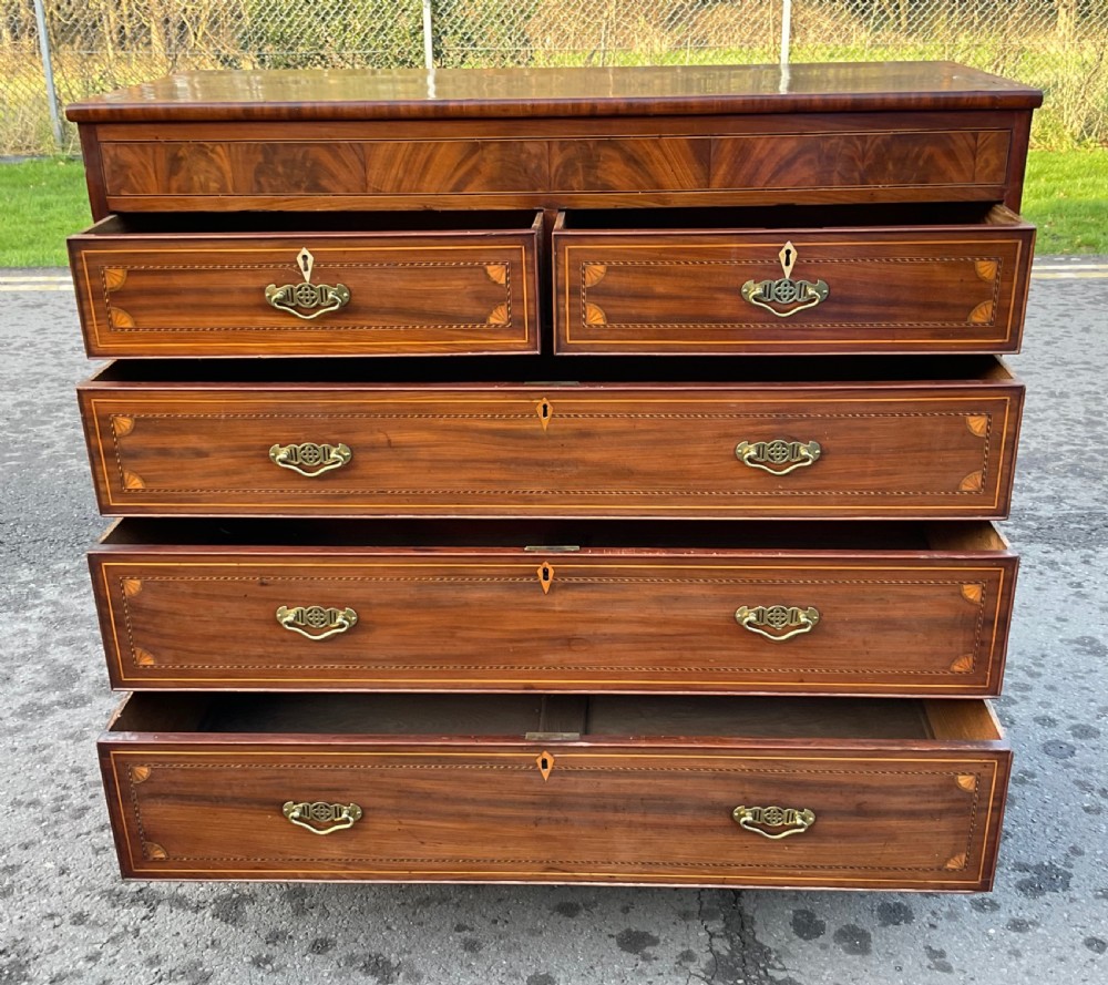 A Georgian mahogany chest of drawers with decorative boxwood inlay, brass handles, and turned foot supports. View VI