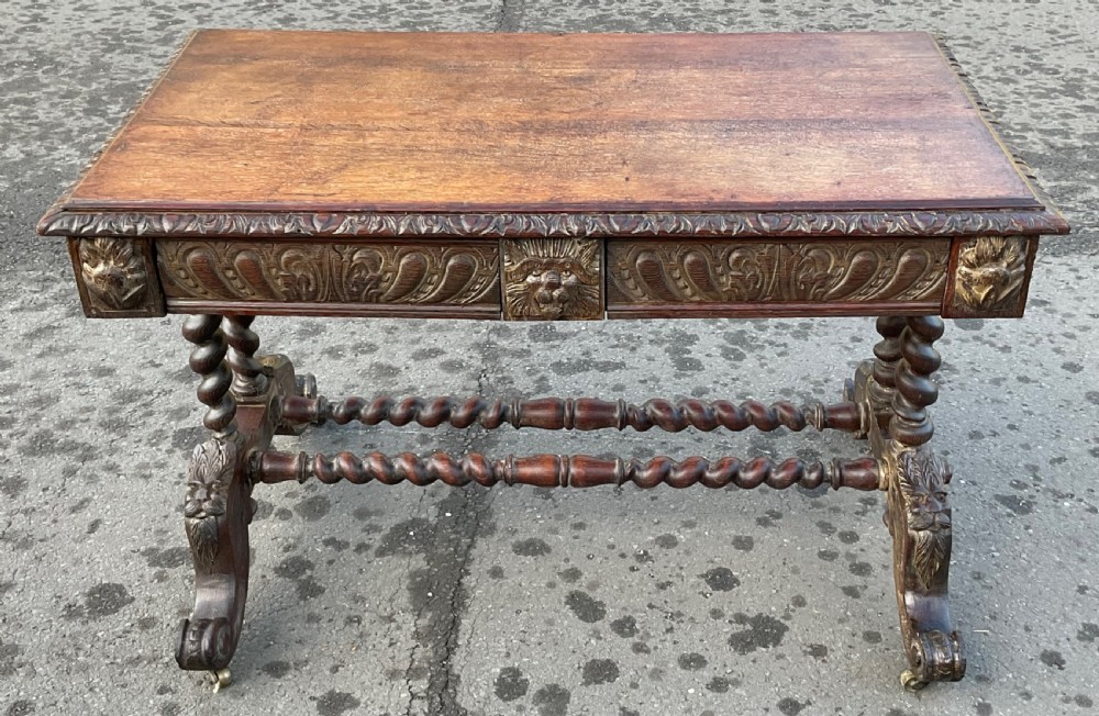 A Victorian dark oak writing table featuring a flat rectangular top, relief-carved frieze with mask motifs, barley twist legs, double stretchers, and brass castors. View VIII
