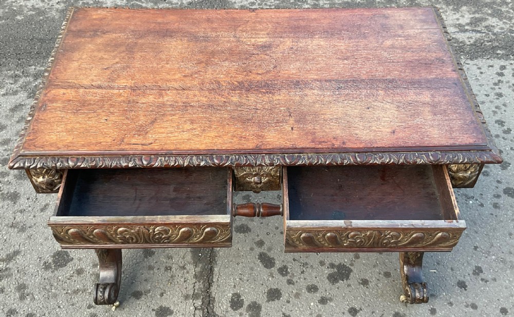 A Victorian dark oak writing table featuring a flat rectangular top, relief-carved frieze with mask motifs, barley twist legs, double stretchers, and brass castors. View XI