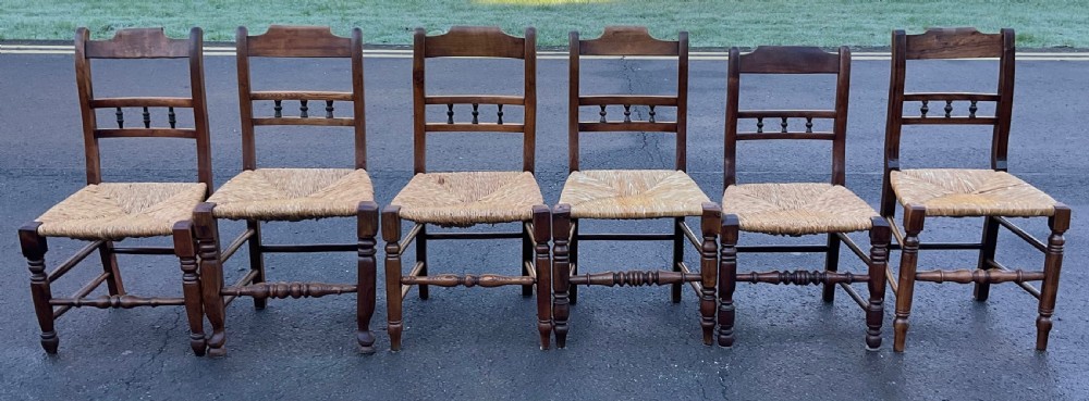 A set of six dark wooden elm dining chairs featuring hand-woven rush seats, turned front stretchers, and spindle back detail.