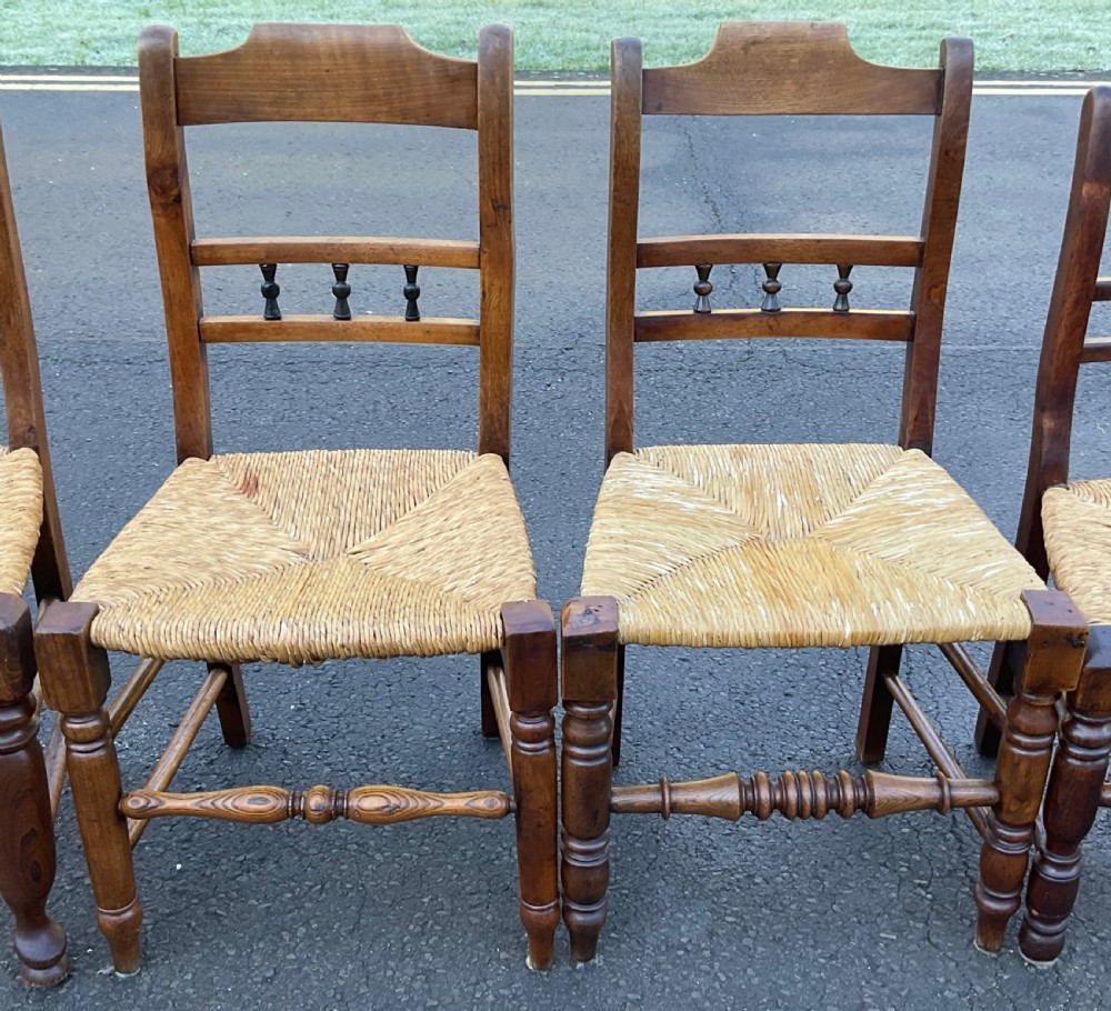 A set of six dark wooden elm dining chairs featuring hand-woven rush seats, turned front stretchers, and spindle back detail. View II