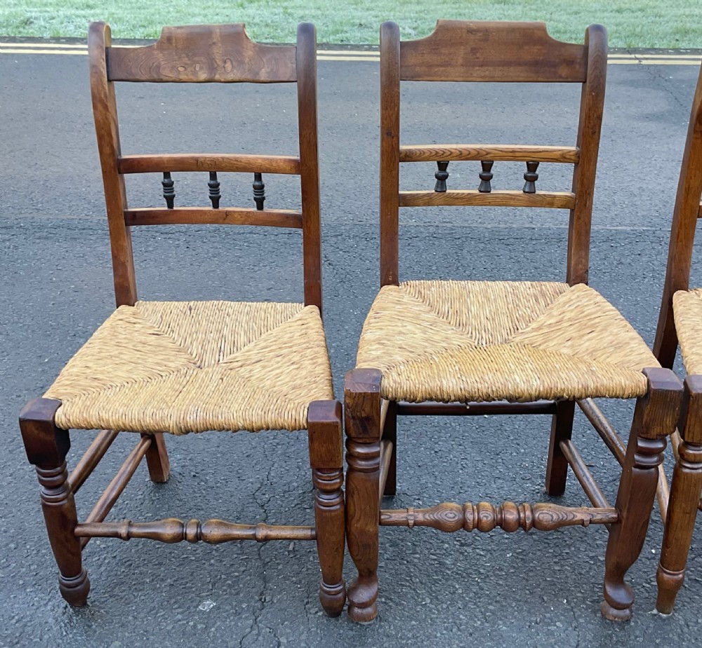 A set of six dark wooden elm dining chairs featuring hand-woven rush seats, turned front stretchers, and spindle back detail. View III