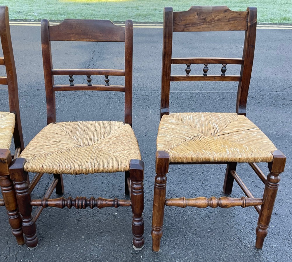 A set of six dark wooden elm dining chairs featuring hand-woven rush seats, turned front stretchers, and spindle back detail. View V