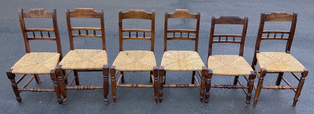 A set of six dark wooden elm dining chairs featuring hand-woven rush seats, turned front stretchers, and spindle back detail. View VI